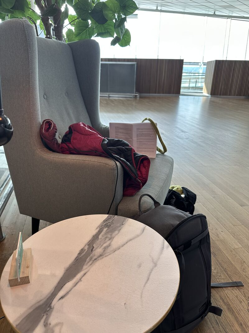 Bagasje og en åpen bok i en lenestol i avgangshallen på Gardermoen lufthavn