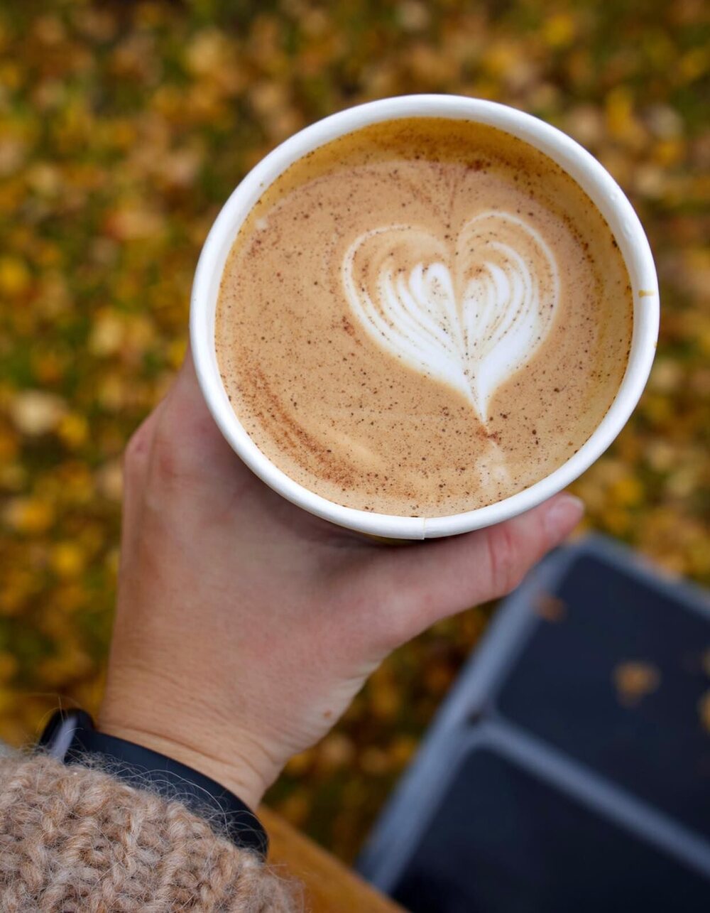 En hånd holder et kaffebeger med et hjerte tegnet i melkeskummet