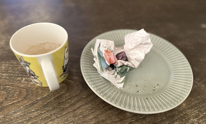 En brukt kaffekopp ved siden av et fat med matrester og en krøllete serviett på et fellesareal
